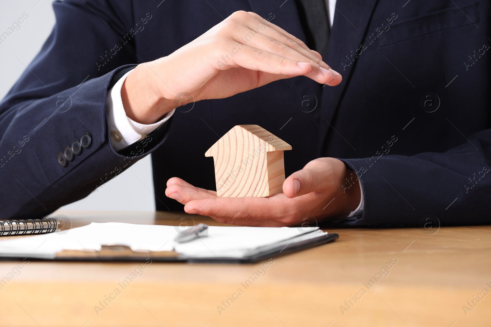 Photo of Property insurance. Real estate agent protecting house figure at table, closeup