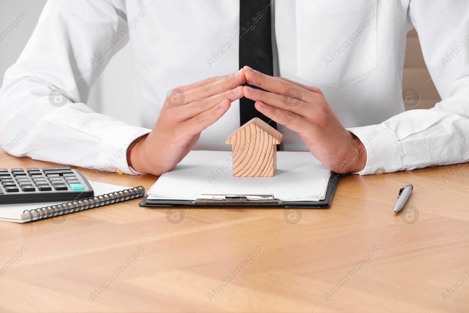 Photo of Property insurance. Real estate agent protecting house figure at wooden table, closeup