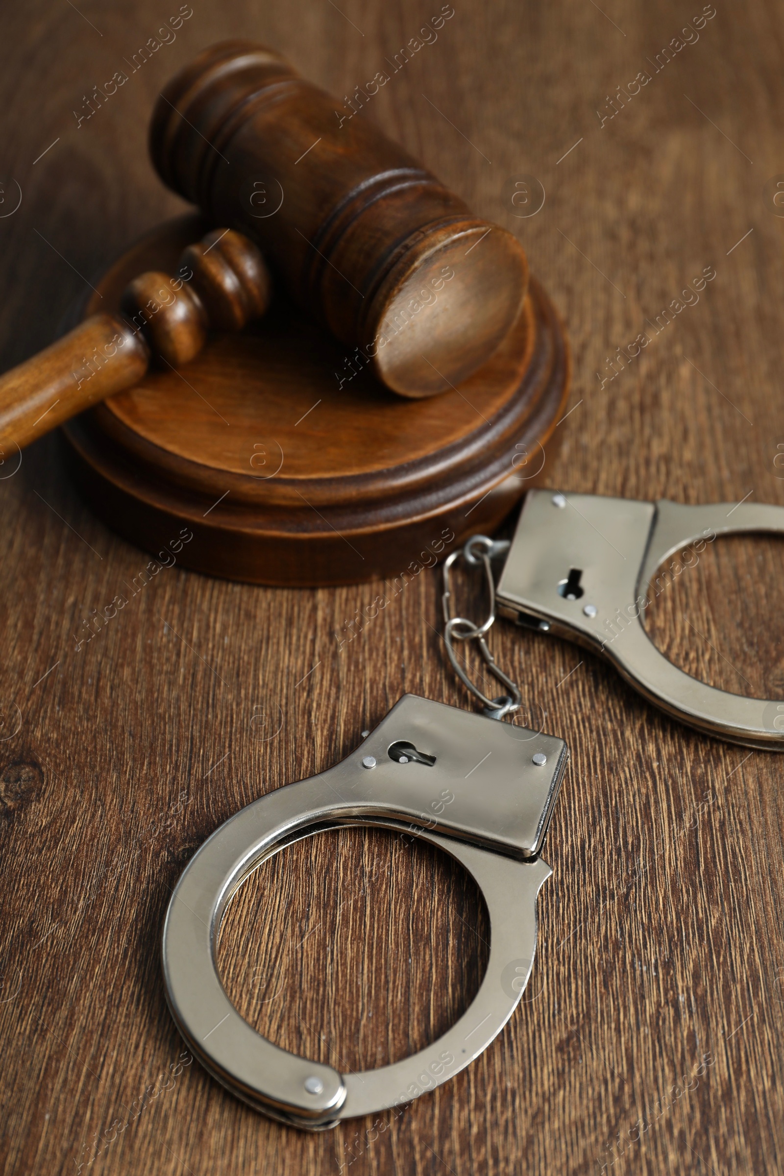 Photo of Handcuffs and judge's gavel on wooden table, closeup