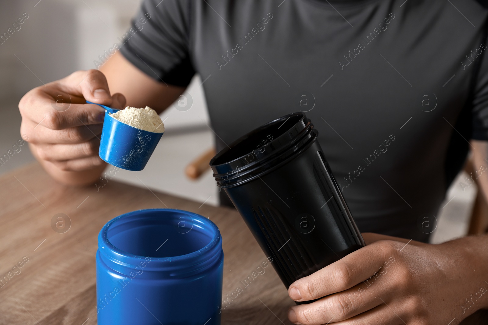 Photo of Making protein cocktail. Man adding powder into shaker at wooden table, closeup