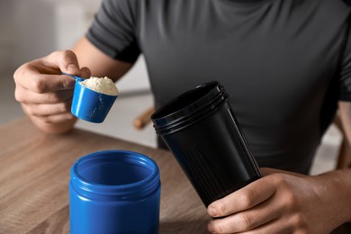 Photo of Making protein cocktail. Man adding powder into shaker at wooden table, closeup