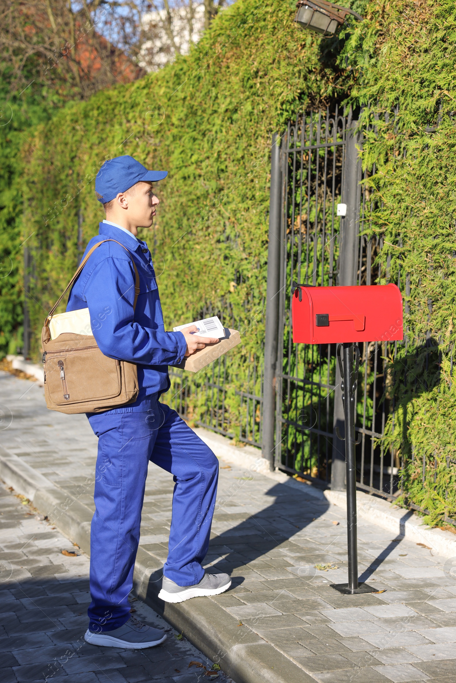 Photo of Postman with parcels near mail box outdoors