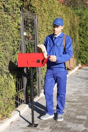 Photo of Postman putting parcel into mail box outdoors