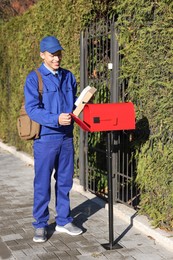 Photo of Postman putting parcel into mail box outdoors