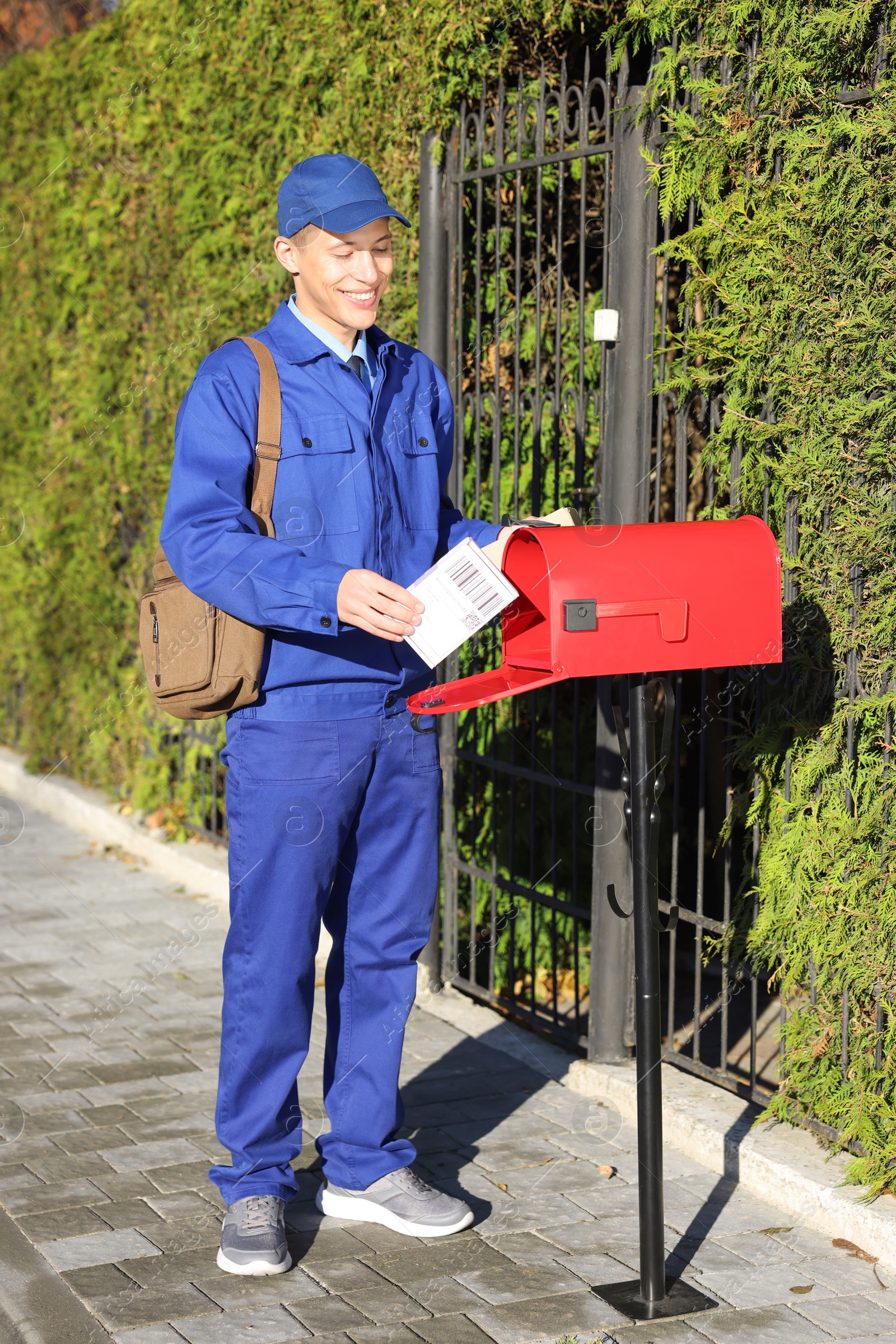 Photo of Postman putting parcel into mail box outdoors