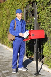 Photo of Postman putting parcel into mail box outdoors