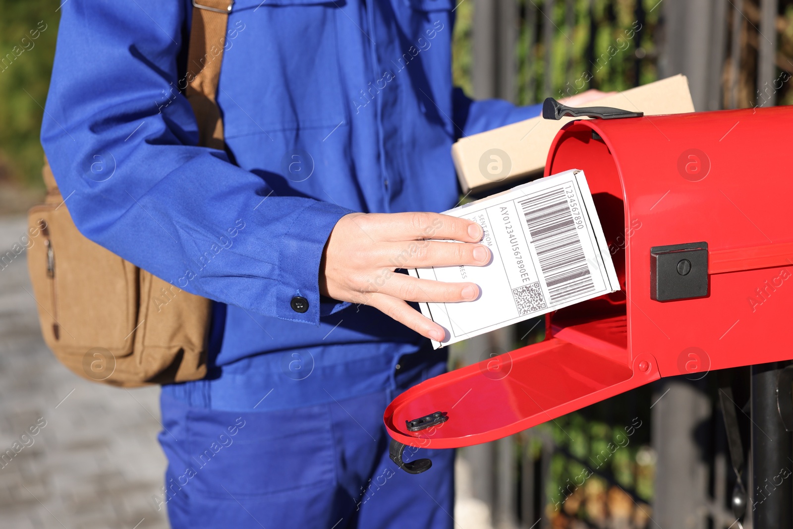 Photo of Postman putting parcel into mail box outdoors, closeup