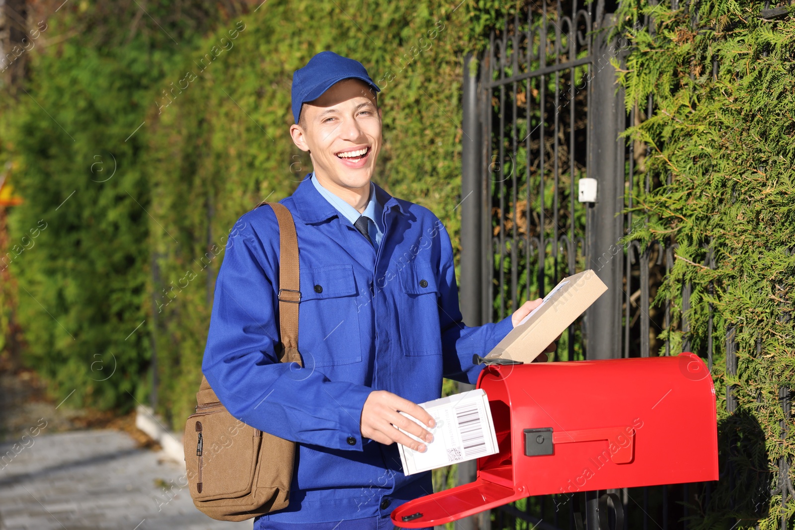 Photo of Postman putting parcel into mail box outdoors