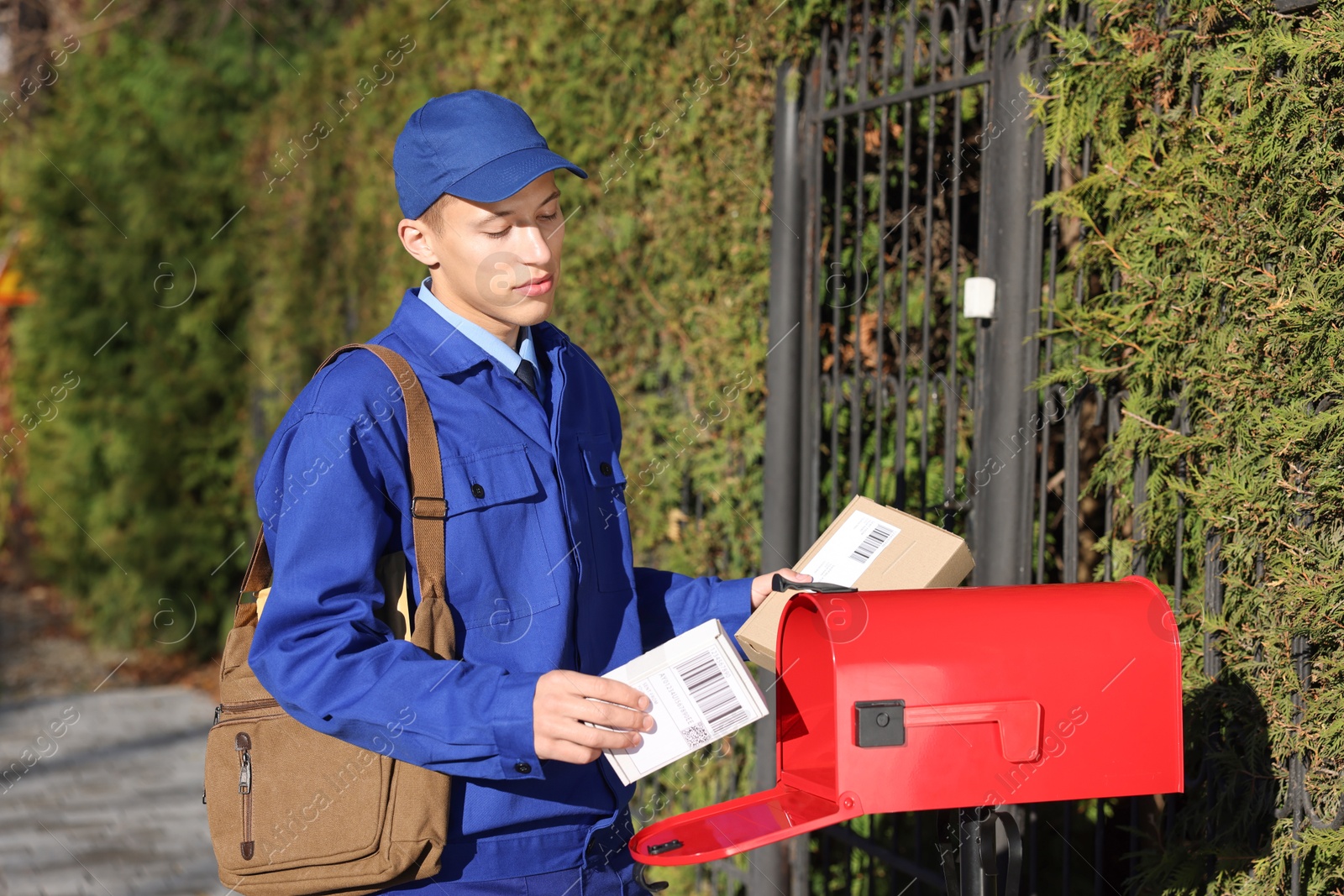 Photo of Postman putting parcel into mail box outdoors