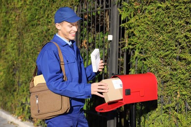 Photo of Postman putting parcel into mail box outdoors