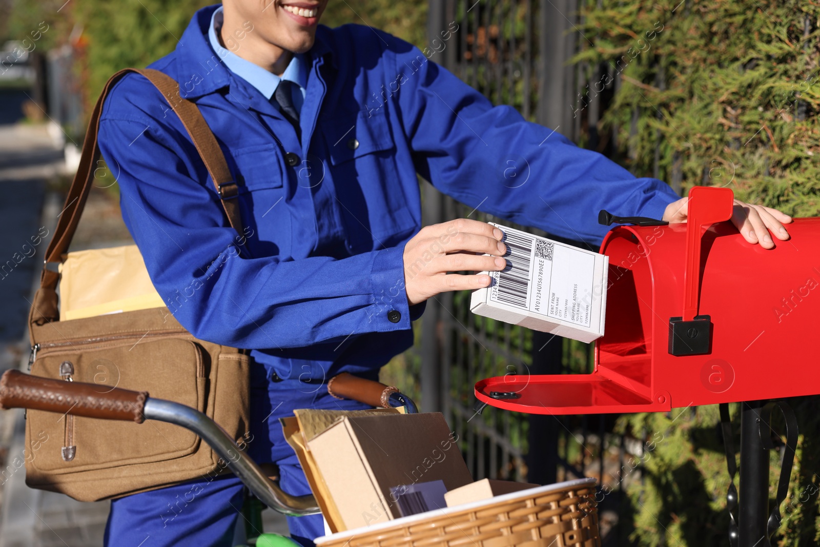 Photo of Postman with bicycle putting parcel into mail box outdoors, closeup