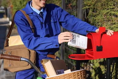 Photo of Postman with bicycle putting parcel into mail box outdoors, closeup