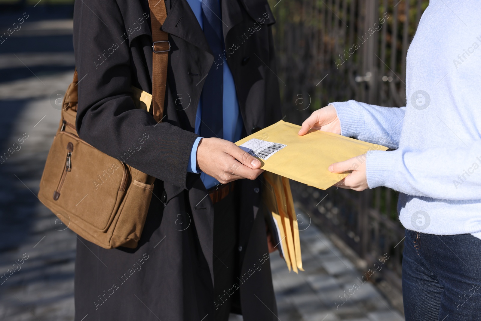 Photo of Postman giving parcel to woman outdoors, closeup