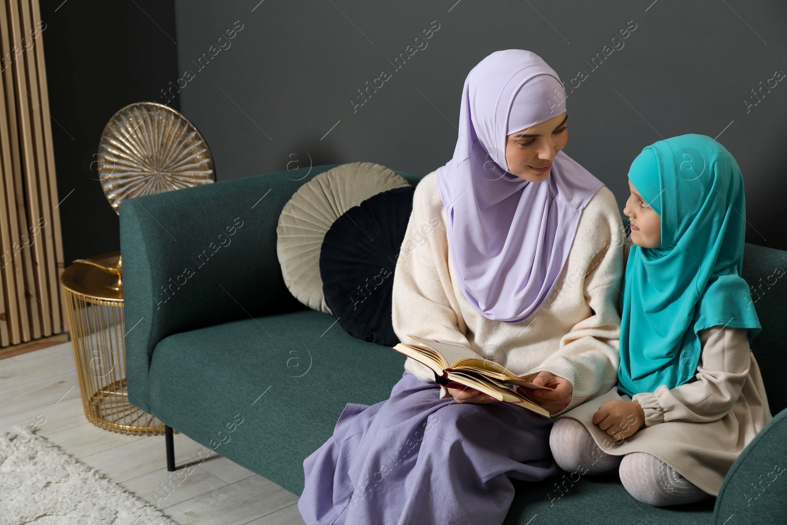 Photo of Muslim woman and her daughter reading Quran at home, space for text