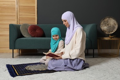 Photo of Muslim woman and her daughter with Quran praying on mat at home