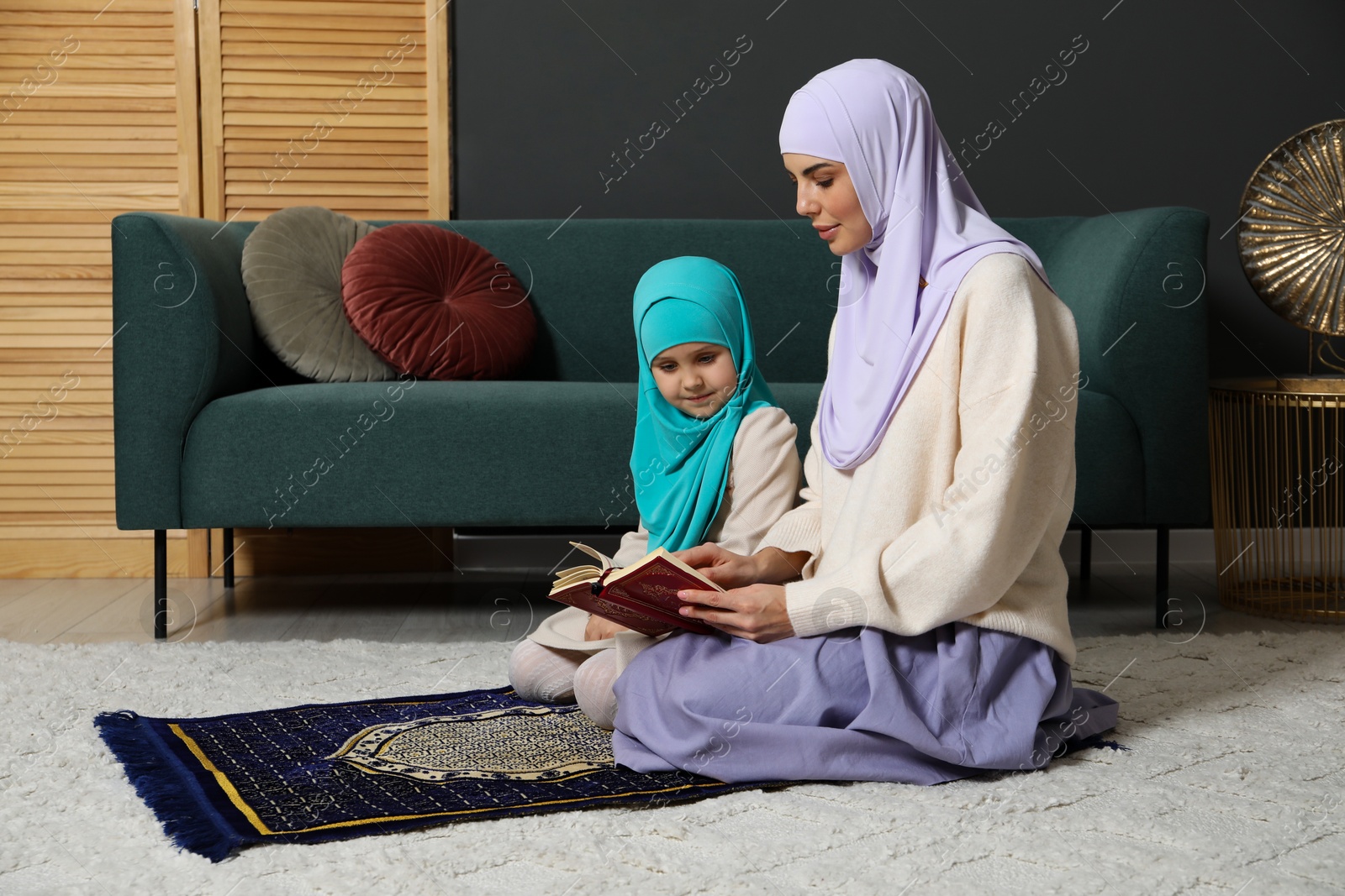 Photo of Muslim woman and her daughter with Quran praying on mat at home