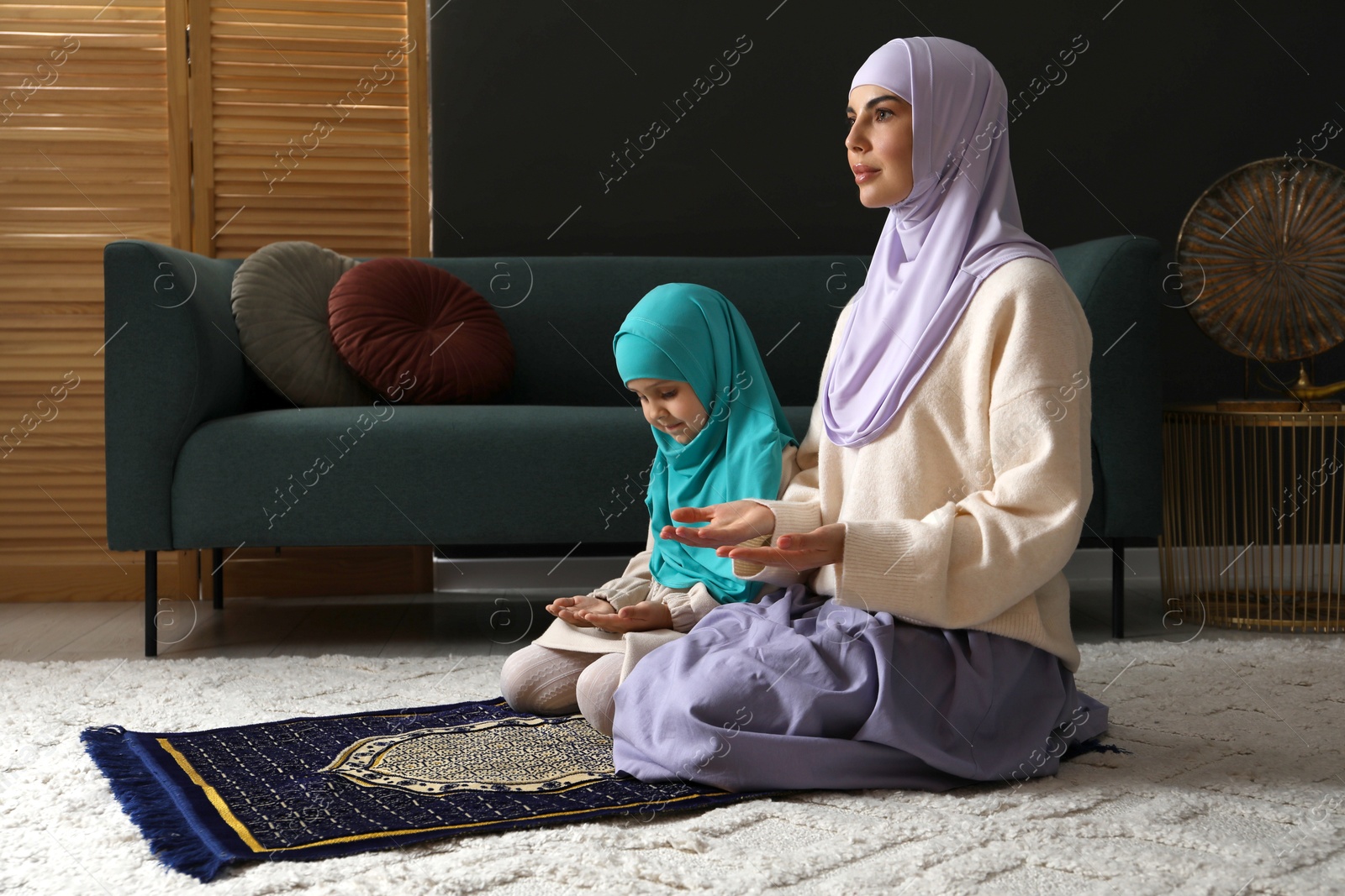 Photo of Muslim woman and her daughter praying on mat at home