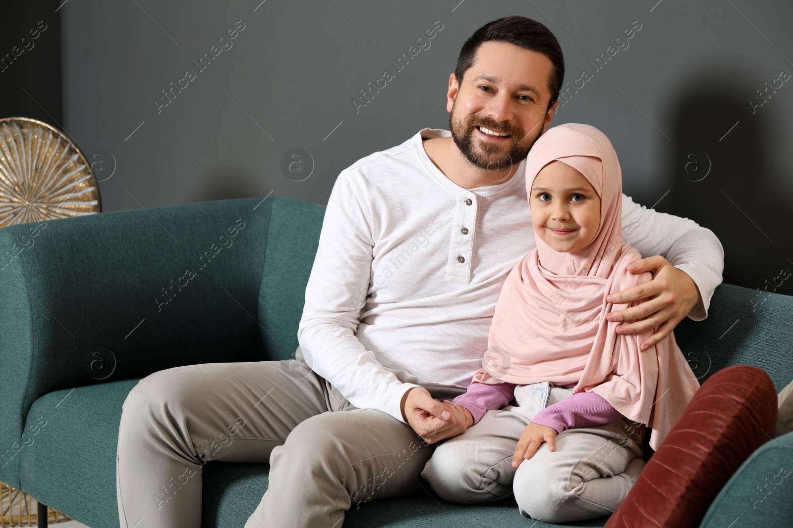 Photo of Muslim man and his daughter sitting on sofa at home