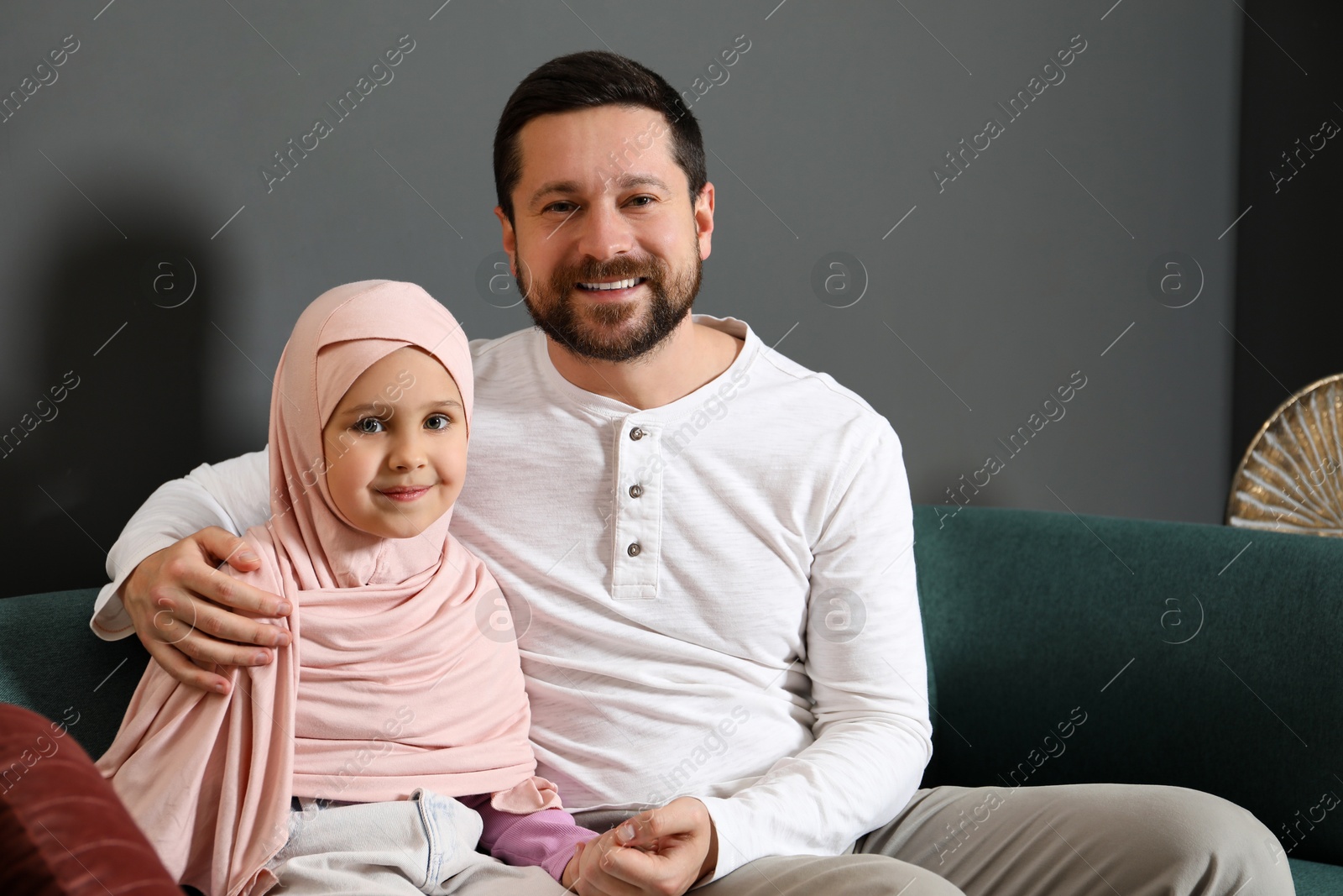 Photo of Muslim man and his daughter sitting on sofa at home