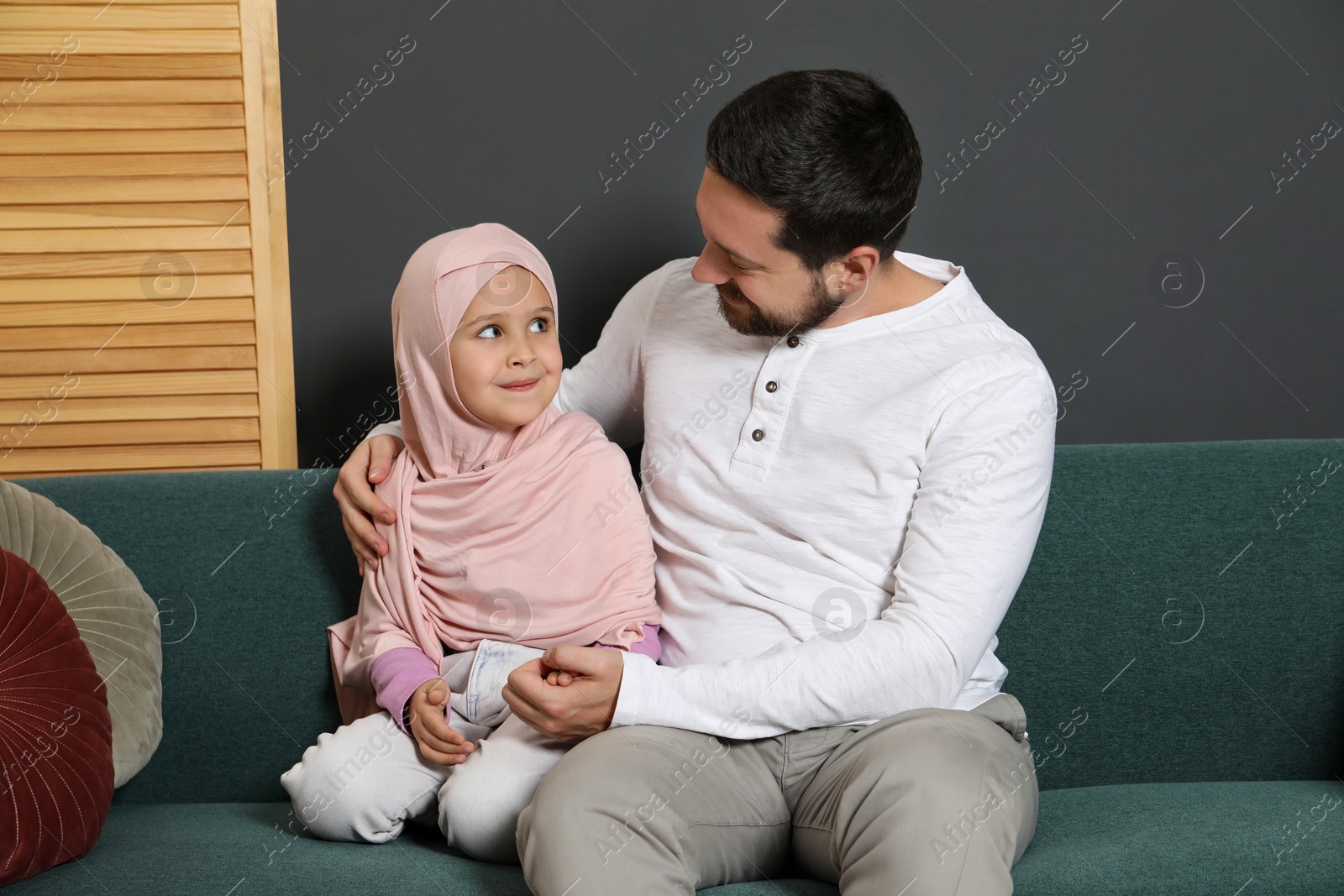 Photo of Muslim man and his daughter sitting on sofa at home