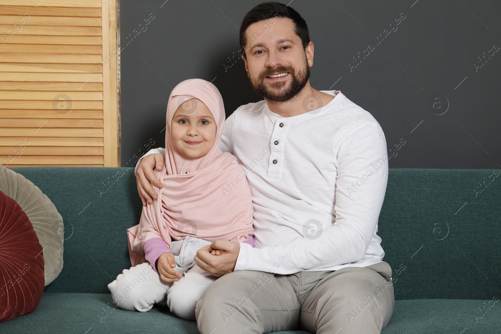 Photo of Muslim man and his daughter sitting on sofa at home