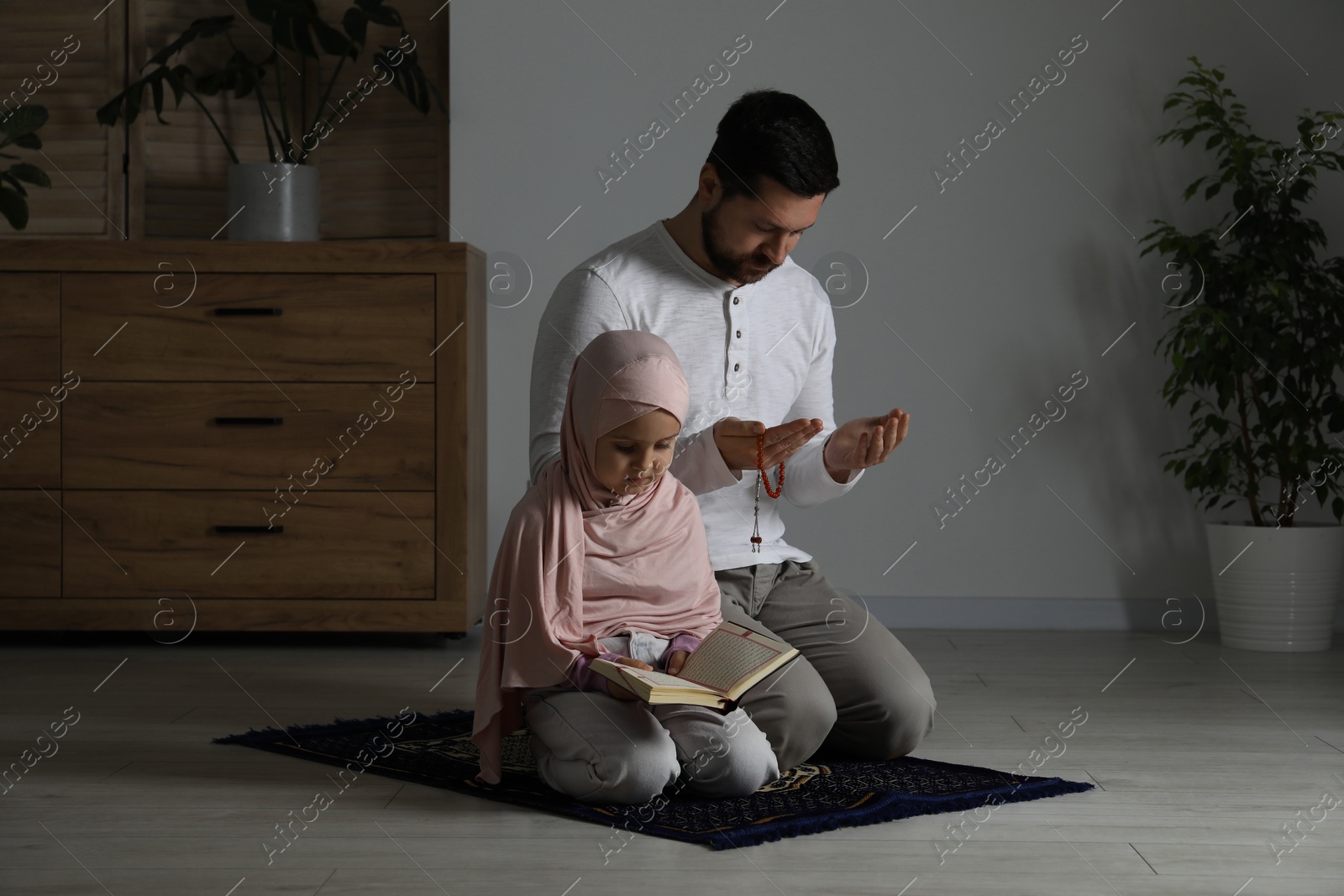 Photo of Muslim man and his daughter with Quran praying on mat at home