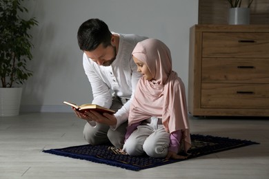 Photo of Muslim man and his daughter with Quran praying on mat at home