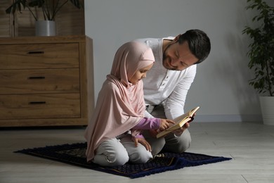 Photo of Muslim man and his daughter with Quran praying on mat at home