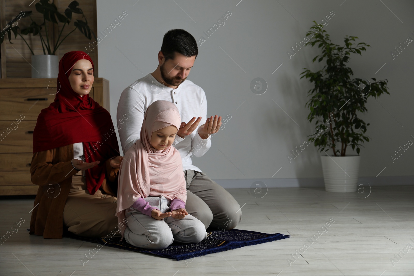 Photo of Muslim family praying on mat at home, space for text