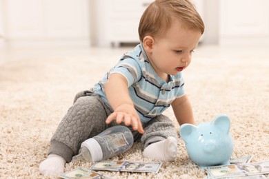 Photo of Little baby with bottle, money and piggybank on floor at home