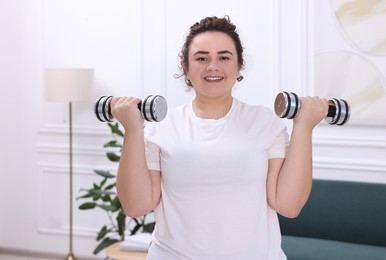 Photo of Plus size woman with dumbbells training at home