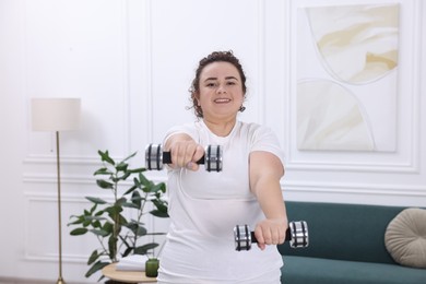 Photo of Plus size woman with dumbbells training at home