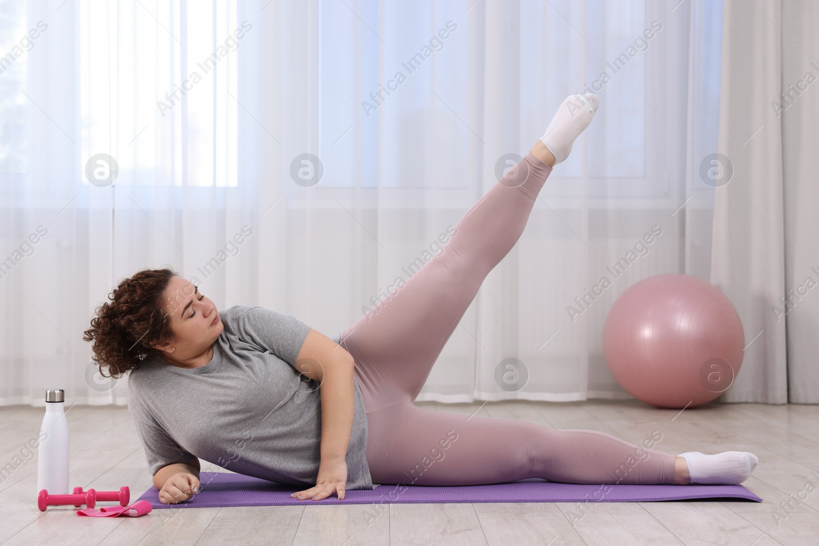 Photo of Plus size woman exercising on fitness mat at home