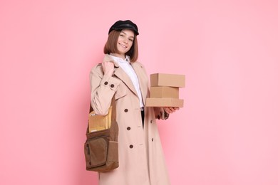 Photo of Happy postwoman with bag and parcels on pink background