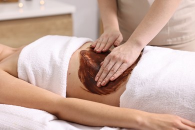 Photo of Woman undergoing chocolate body wrap treatment in spa salon, closeup