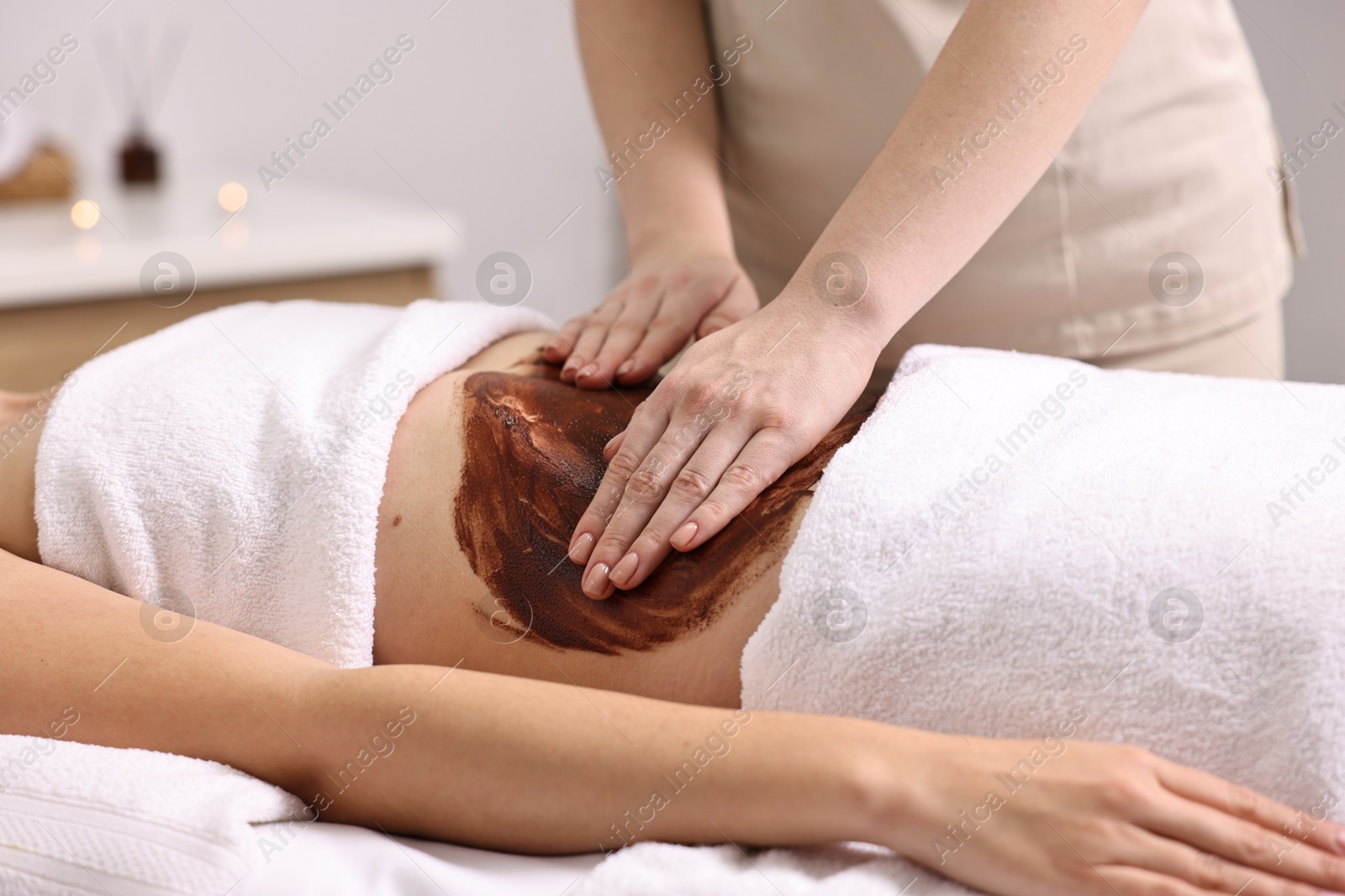 Photo of Woman undergoing chocolate body wrap treatment in spa salon, closeup