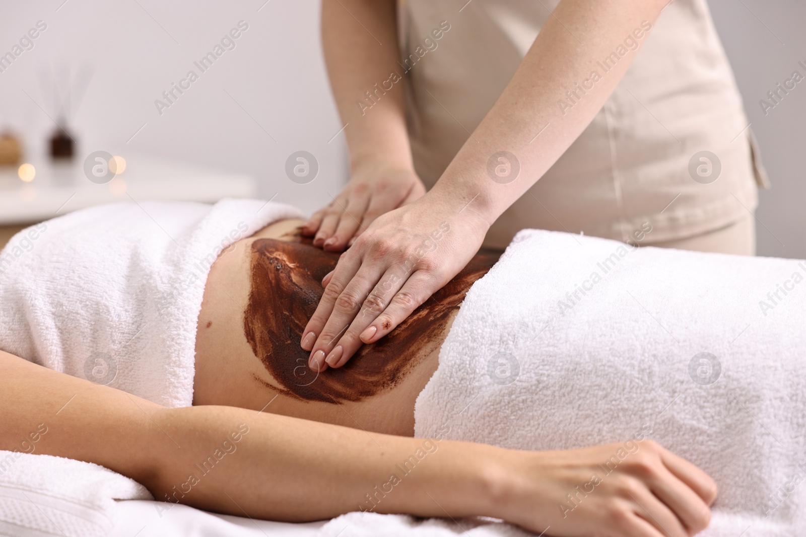 Photo of Woman undergoing chocolate body wrap treatment in spa salon, closeup