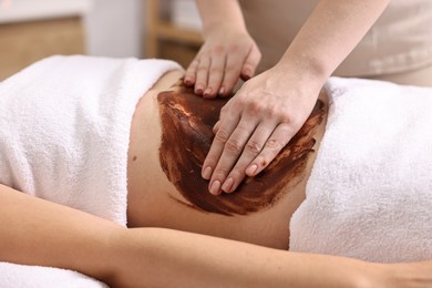 Photo of Woman undergoing chocolate body wrap treatment in spa salon, closeup