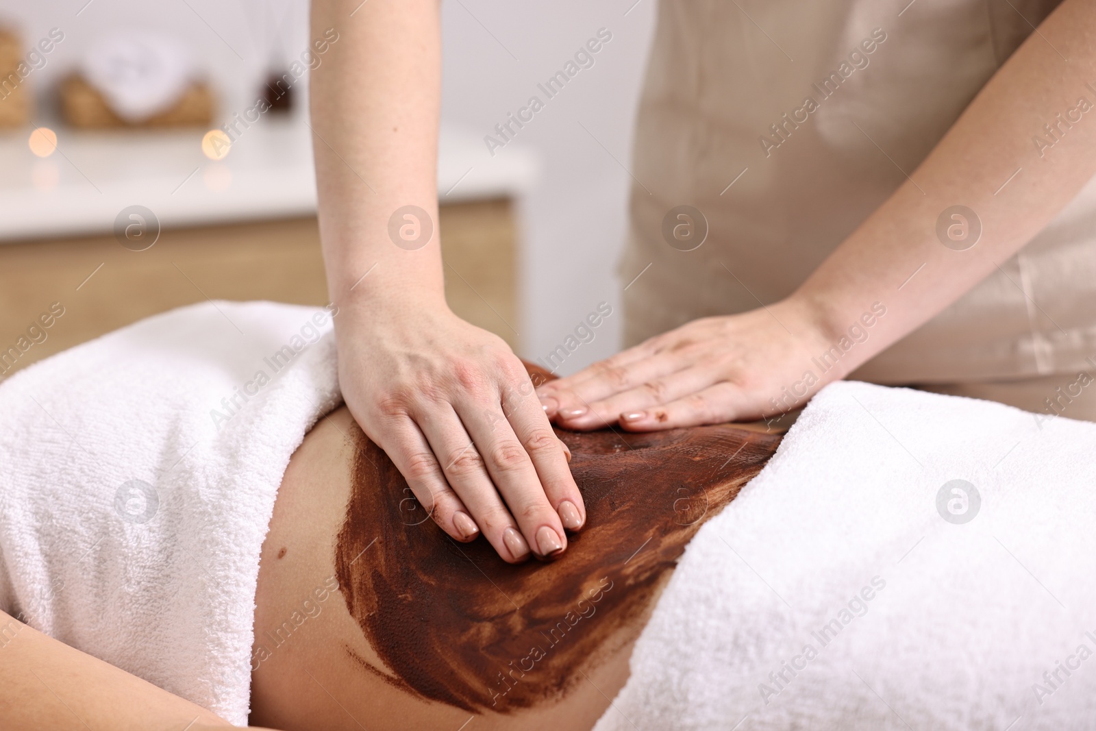 Photo of Woman undergoing chocolate body wrap treatment in spa salon, closeup