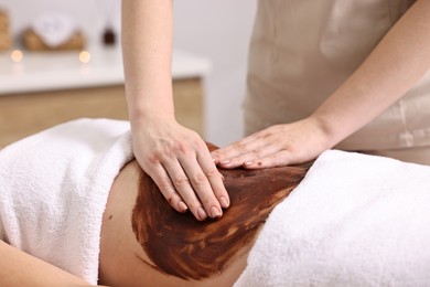 Photo of Woman undergoing chocolate body wrap treatment in spa salon, closeup