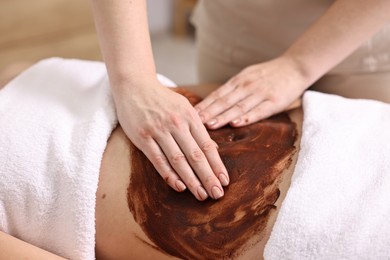 Photo of Woman undergoing chocolate body wrap treatment in spa salon, closeup