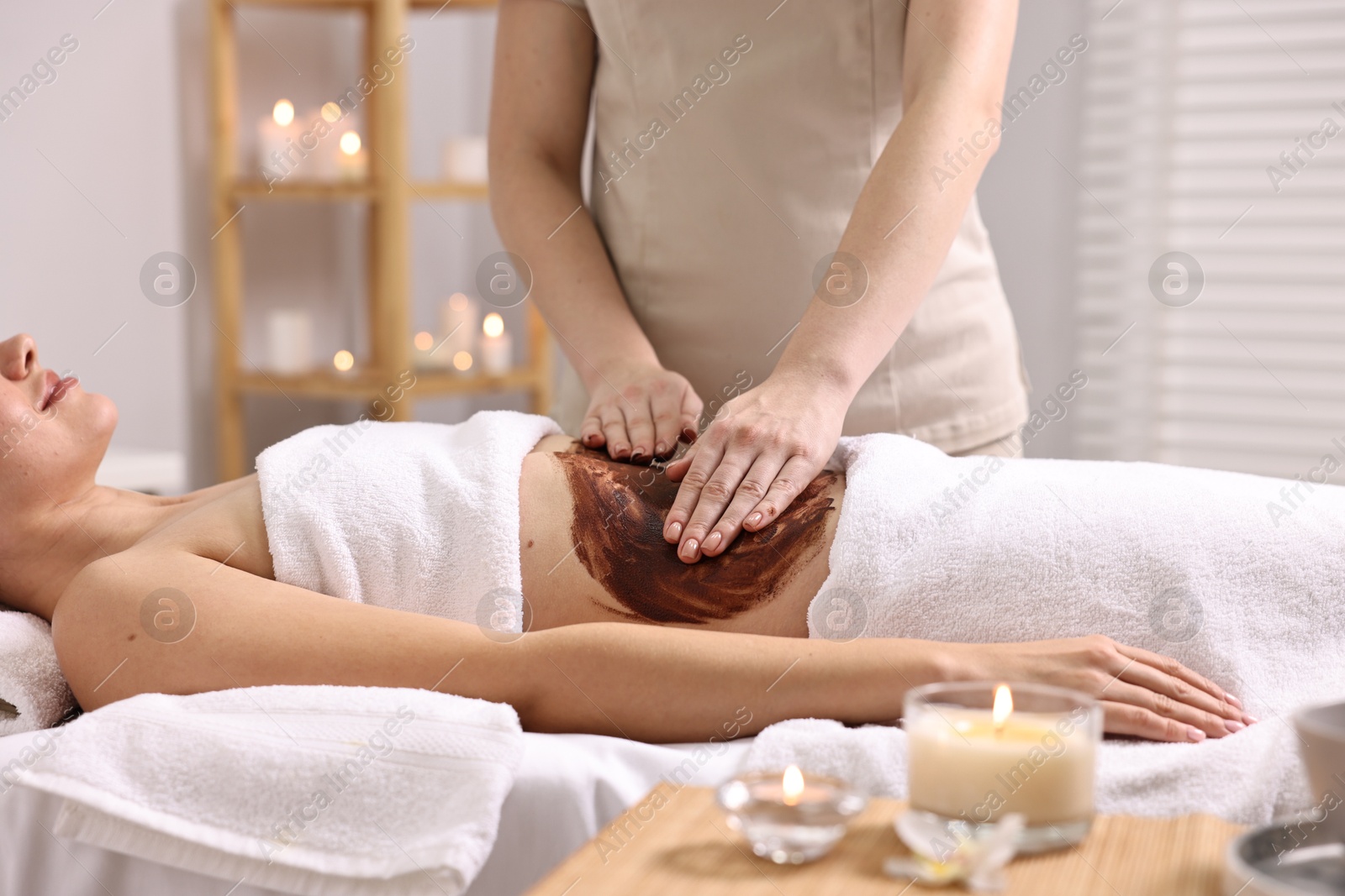 Photo of Woman undergoing chocolate body wrap treatment in spa salon, closeup