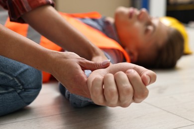 Photo of First aid. Woman checking pulse of her unconscious colleague indoors, closeup