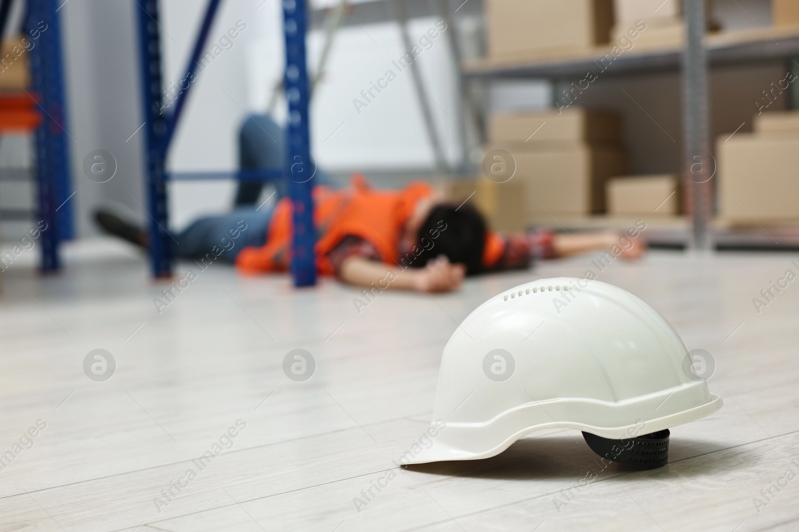 Photo of Accident at work. Hardhat on floor and unconscious woman in warehouse, selective focus