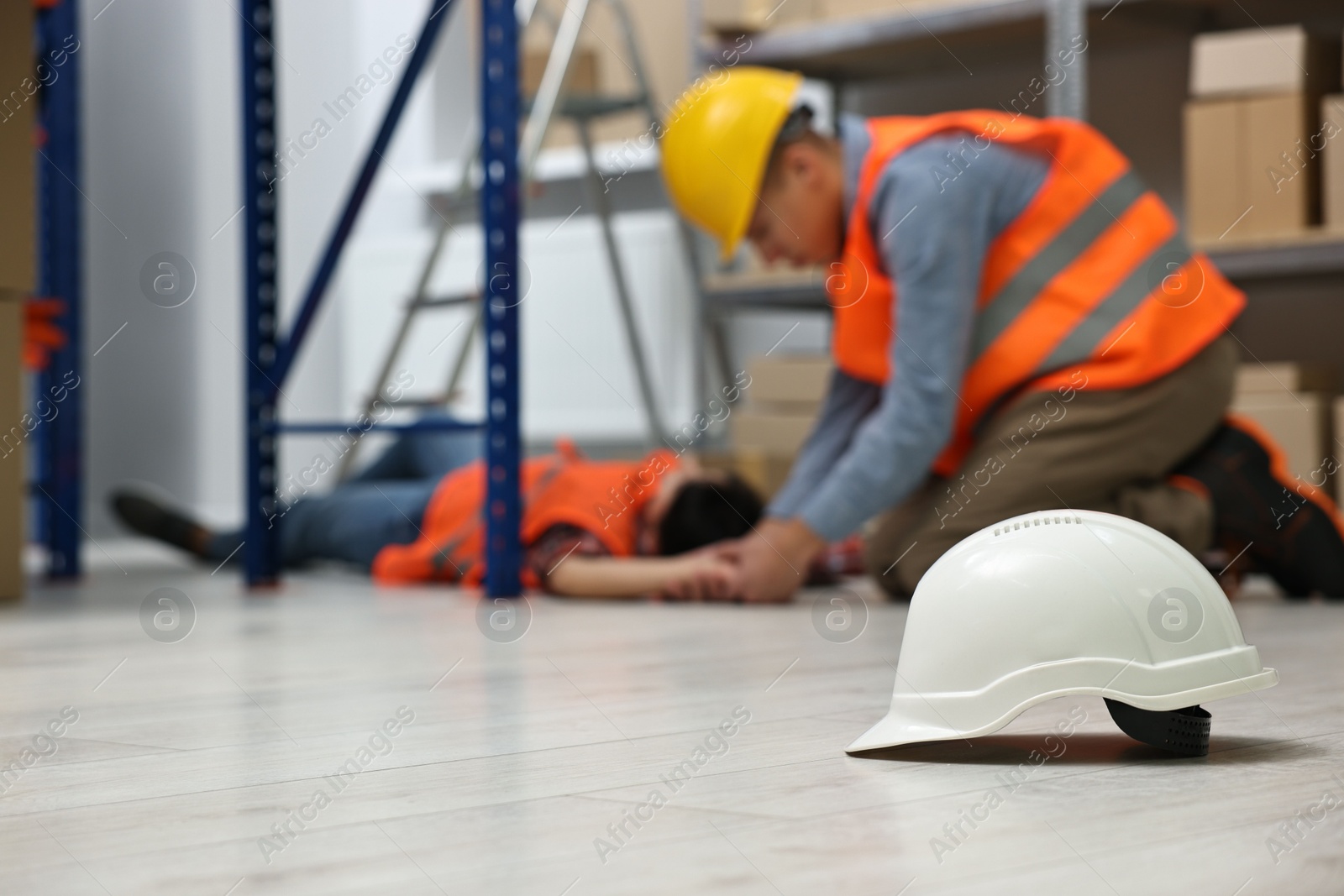 Photo of First aid. Hardhat on floor and man helping his unconscious colleague in warehouse, selective focus