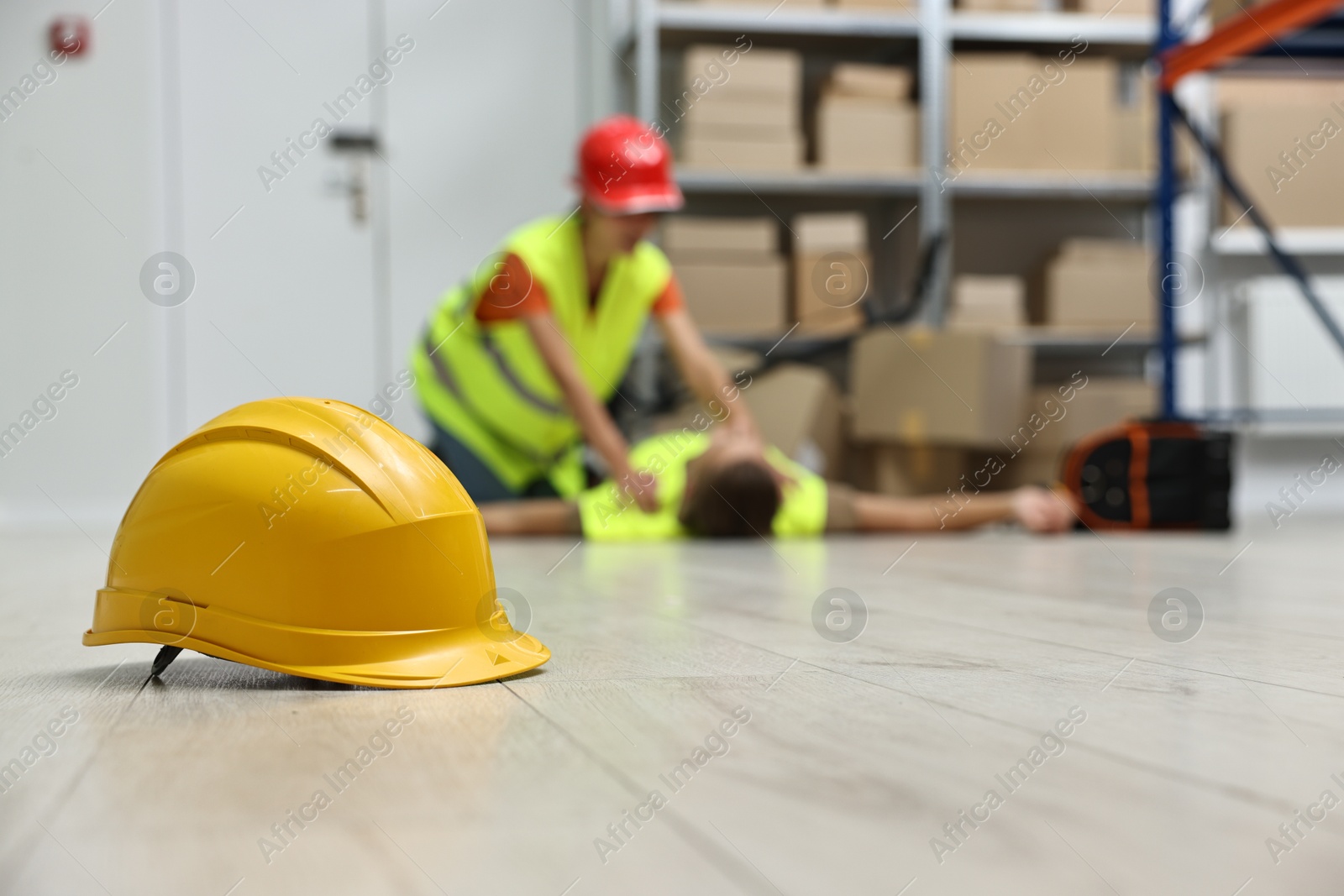 Photo of First aid. Hardhat on floor and woman helping her unconscious colleague in warehouse, selective focus