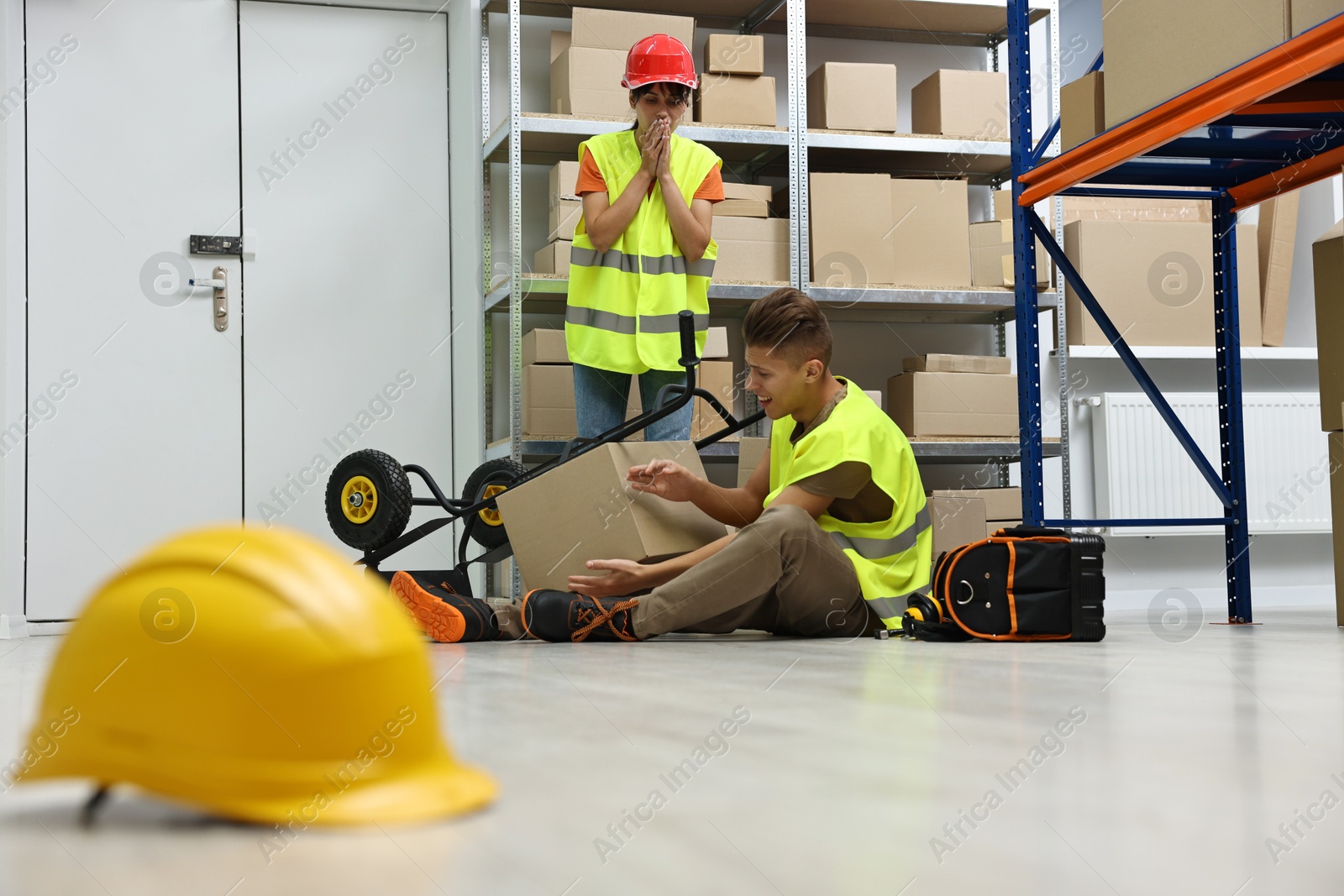 Photo of Accident at work. Worried woman and her injured colleague in warehouse