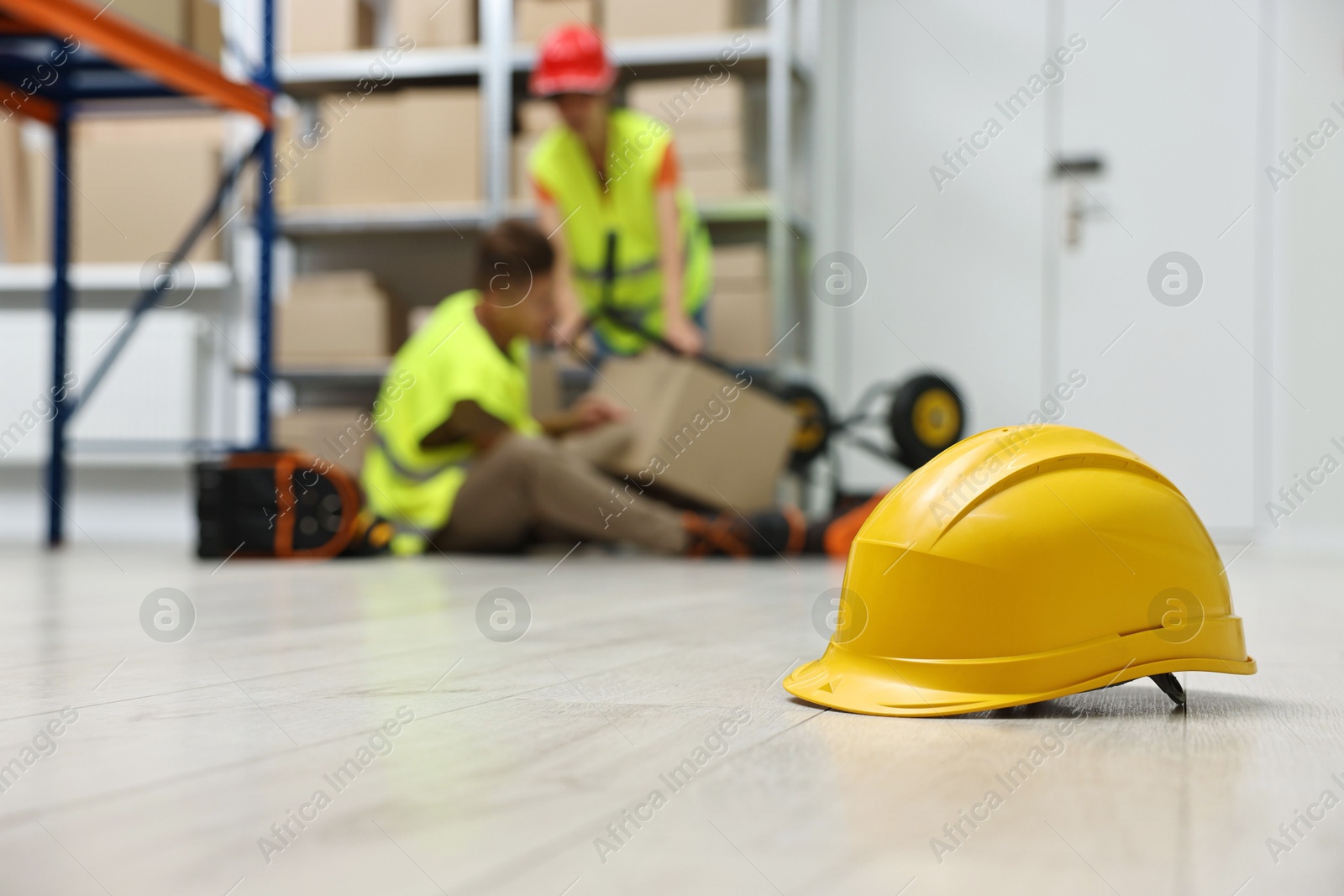 Photo of First aid. Hardhat on floor and woman helping her injured colleague in warehouse, selective focus