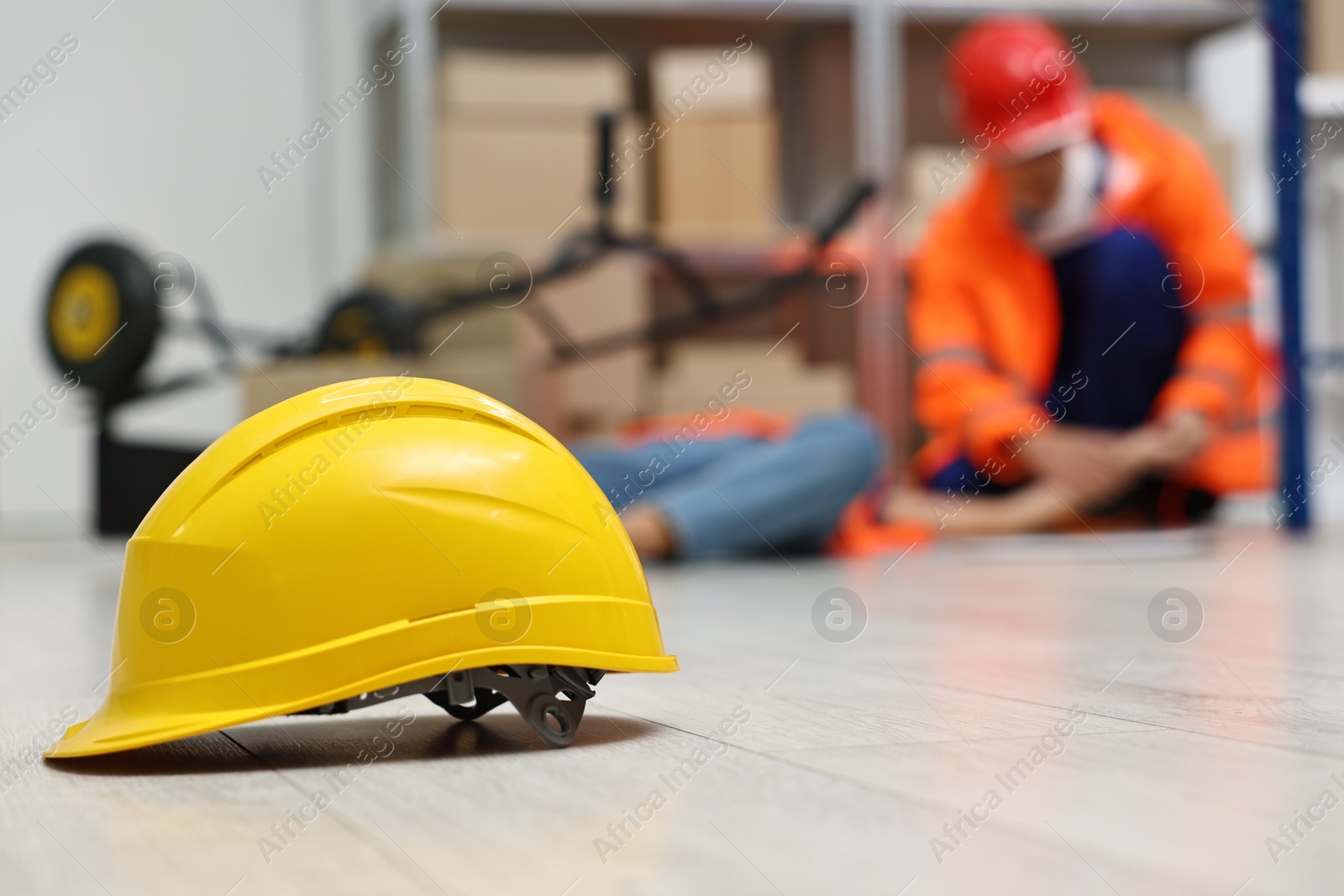 Photo of First aid. Hardhat on floor and man helping his unconscious colleague in warehouse, selective focus