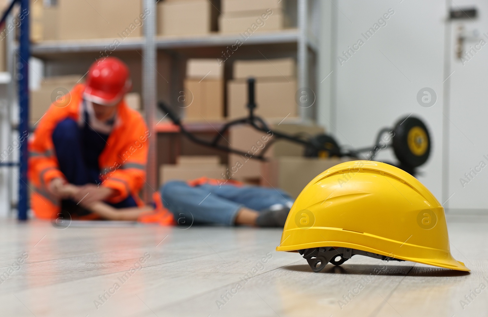 Photo of First aid. Hardhat on floor and man helping his unconscious colleague in warehouse, selective focus